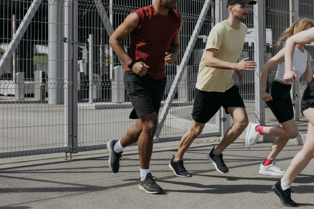 Energetic group of people running together outdoors under bright sunlight, wearing comfortable sportswear.